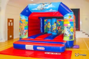 A bouncy castle featuring a police car on top, adorned with vibrant Lego-themed artwork and building block designs.