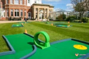 A 9-hole miniature golf course set in front of a grand mansion, featuring colorful obstacles and lush landscaping.