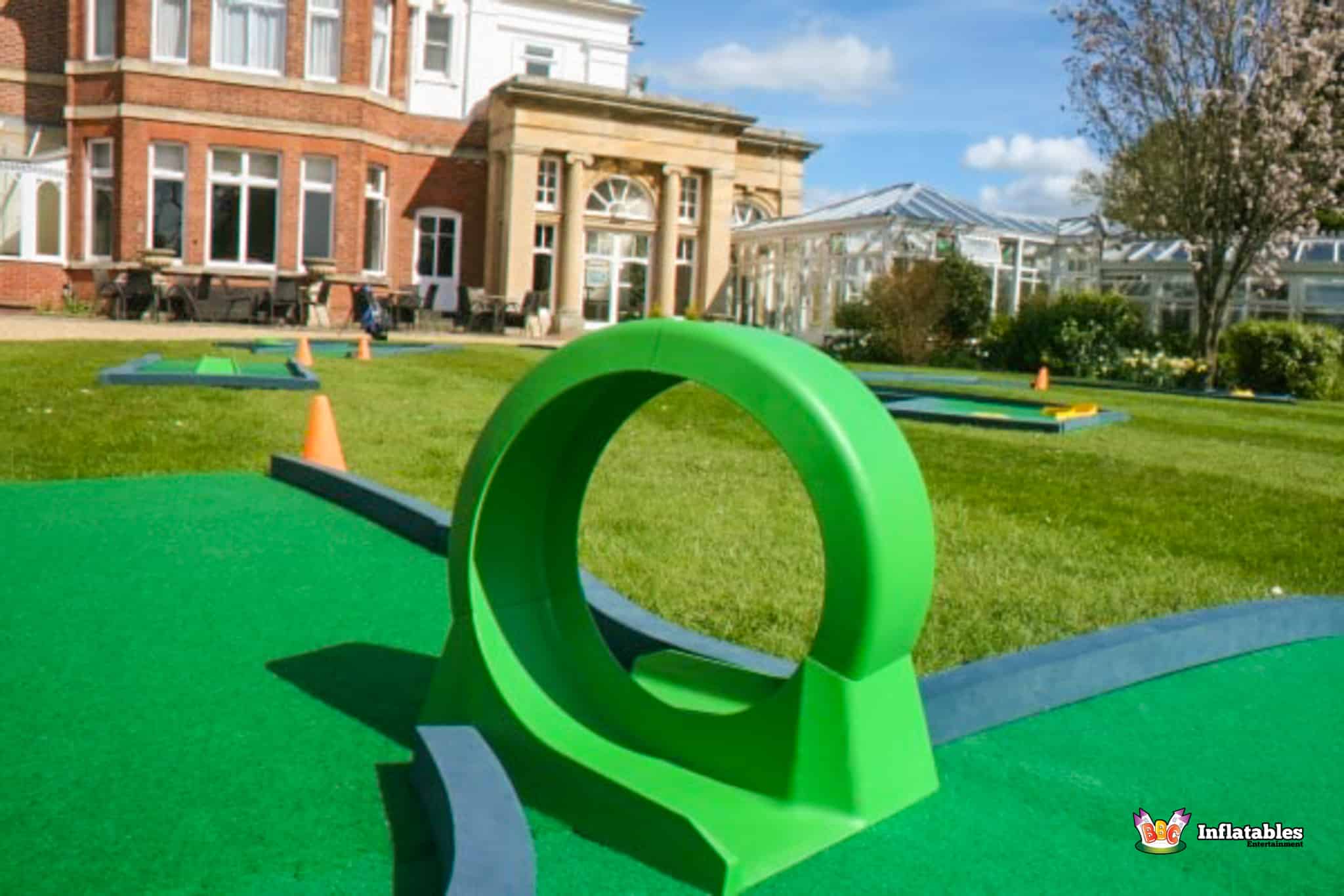 A vibrant crazy golf course located in front of an elegant mansion, showcasing fun obstacles and greenery.