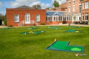 A green lawn featuring a mini golf course with colourful holes and a house in the background.