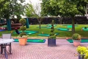 A vibrant green lawn with a 9-hole mini golf setup and a charming house nearby.