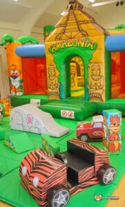A colourful inflatable play area themed "Amazonian," featuring a bouncy castle, slides, and toy cars for children.