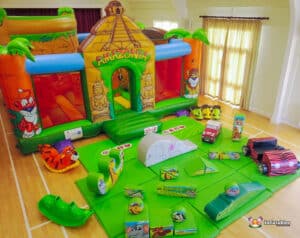 A colorful inflatable bounce house themed "Amazonia" with various cartoon animal designs and play equipment on a green mat.