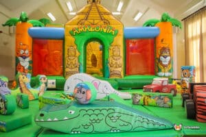 A vibrant indoor bounce house themed "Amazonia," featuring jungle animals and inflatable obstacles, perfect for children's play.