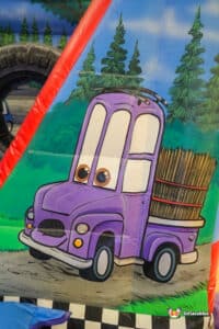 A purple truck sits atop a colorful bounce house labeled "Auto Bouncer," inviting children to play and jump.