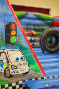 A vibrant bouncy castle designed as cars, complete with a tire, named "Auto Bouncer" for kids to enjoy.