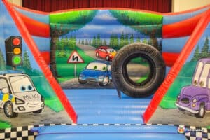 A playful bouncy castle resembling cars and a tire, titled "Auto Bouncer," inviting children to jump and play.