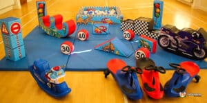 A colorful kids' play area featuring toy vehicles, traffic signs, and soft obstacles on a mat, designed for active play and learning.