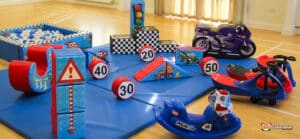 A colorful indoor play area featuring soft toys, traffic signs, and ride-on vehicles designed for children's active play and learning.