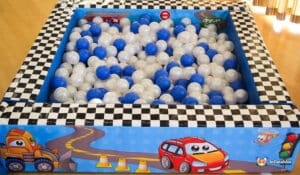 A colorful ball pit filled with blue and white balls, surrounded by a checkered border and playful car graphics. Perfect for kids' playtime.
