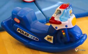 A blue children's rocking police motorcycle toy with colorful buttons and a '911' badge, set on a wooden floor.