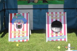 Two carnival games: "Feed the Clown" with a clown face and hole, and "Ball in the Bucket" featuring a bucket, both set on green grass.