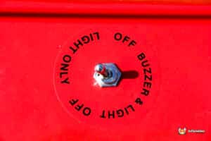 Close-up of a red control panel featuring a toggle switch labeled "LIGHT & BUZZER OFF ONLY," mounted on a circular base.