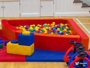 A colorful ball pit surrounded by soft foam blocks and play equipment in a spacious indoor play area.