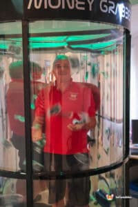 A man in front of a glass wall filled with cash, illustrating the theme of a cash grabber.