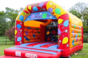 Colorful inflatable bouncy castle with balloons and stars, set against a green landscape. Perfect for children's parties.