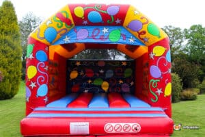 A colorful inflatable bouncy castle with balloons and stars design, set up on a grassy lawn, ready for children's entertainment.