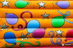 Colorful balloons and stars adorn a vibrant orange inflatable surface, adding a festive touch to a playful environment.