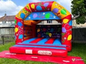 Colourful inflatable bouncy castle with balloons and stars, set on green grass, ready for fun activities. Ideal for children's parties.