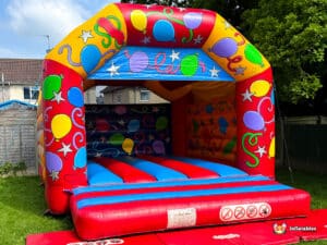 A colorful bouncy castle with balloons and stars design, set in a grassy backyard, ready for kids to play and have fun.