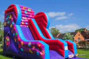 A large inflatable slide decorated with colorful candy and balloons, titled "Celebrations Slide," perfect for festive events.