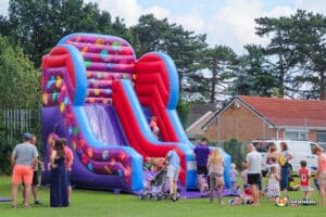 Slide features a large inflatable slide adorned with vibrant candy and balloons, ideal for parties.