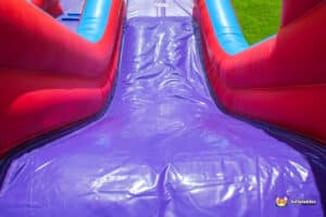 The Slide" features a colourful purple and red inflatable design, perfect for outdoor fun and play.