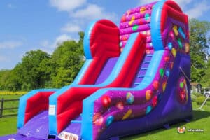 "Celebrations Slide" is a large inflatable slide, cheerfully decorated with candy and balloons, inviting everyone to enjoy.