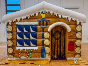 Front view of the inflatable Christmas Grotto, showing the wood-grain texture, snow-covered roof, golden curtained entrance, and a red "Letters" mailbox.