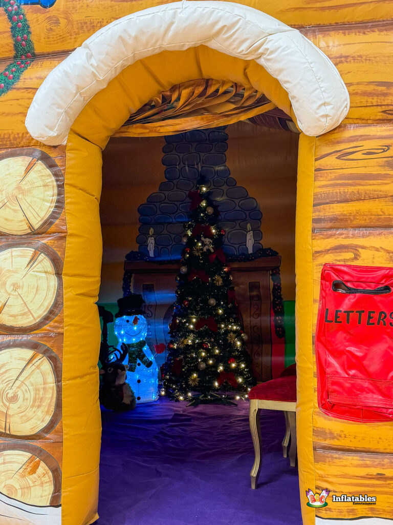 Close-up shot through the arched entrance of the grotto, showing a glowing Christmas tree and light-up snowman inside against a background painted with a stone fireplace.