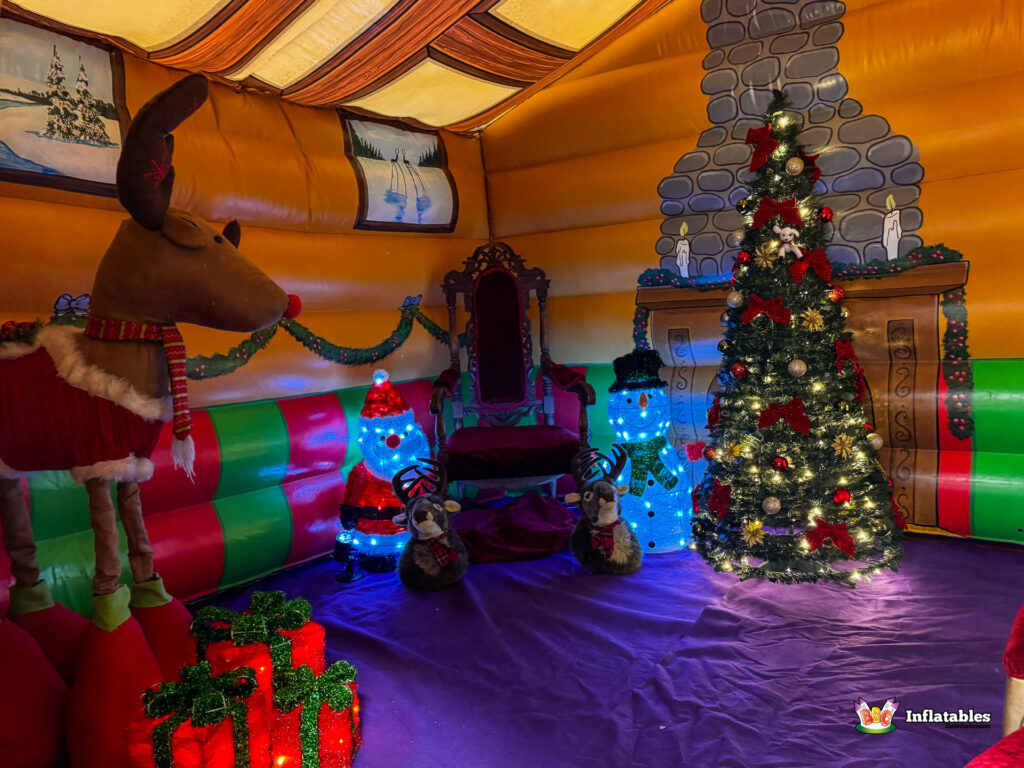 Interior view of the illuminated Christmas Grotto, featuring a red Santa's throne, a tall decorated Christmas tree, a large reindeer prop, and light-up Santa and snowman figures.