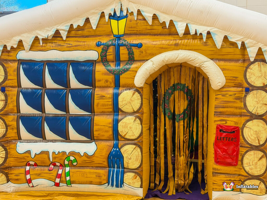 Close-up of the highly detailed front artwork of the inflatable grotto, focusing on the log-cabin texture, painted windows, and the entryway with the wreath and mailbox