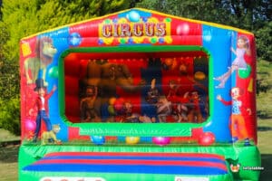 A colorful bouncy castle featuring a clown and a clown's face, surrounded by a pool of circus balls.