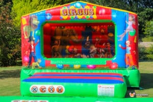 A vibrant bouncy castle with a clown and a clown's face, set against a backdrop of a circus ball pool.