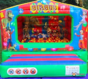 A cheerful bouncy castle displaying a clown and a clown's face, with a playful circus ball pool nearby.