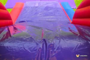 Close-up of a colorful inflatable water slide featuring red, blue, and purple surfaces, ready for children's fun in a grassy area.