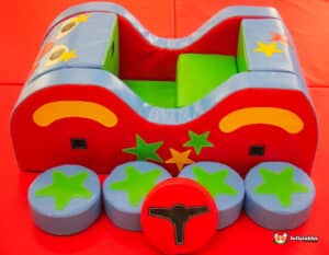 A colorful toy car with a red and blue seat and a green and blue seat, located in a circus-themed soft play space.