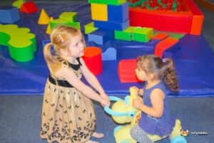 Children joyfully playing in a colorful block play area, surrounded by soft play equipment and a ball pool.