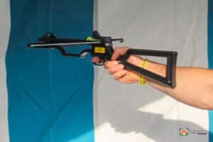A hand holds a black slingshot-like device against a blue and white background, showcasing its design and grip.