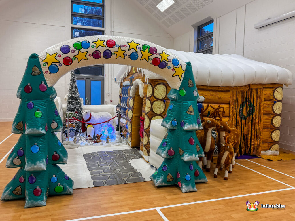 Frontal view of the full attraction set up indoors, showing the log cabin grotto, the plush reindeer figures, the festive archway, and the snowy scene with the polar bear.
