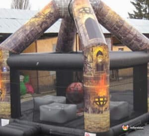Inflatable castle with a fire pit and a wrecking ball, set against a bright blue sky, creating a playful atmosphere.