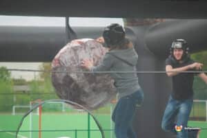 Two people play on a large inflatable wrecking ball, laughing and enjoying their time together outdoors.