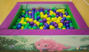A colorful ball pit in purple and green, topped with a friendly dinosaur, designed for fun in the Dino Soft Play zone.