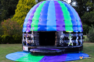 A colorful inflatable dome with blue, green, and purple stripes, featuring dancing silhouettes and a welcoming entrance.