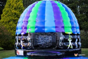 Colorful inflatable dome with blue, green, and purple stripes, featuring silhouettes of dancers and music symbols on a black base.