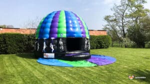 A colorful inflatable dome with a blue and green top, featuring dance graphics, set on a grassy lawn.