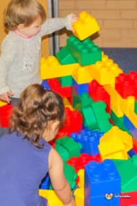 Two children happily constructing structures with Edublocks Lego blocks on a vibrant play surface.