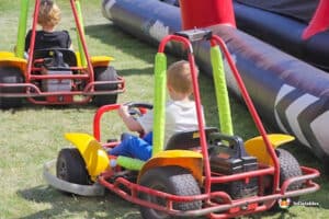 Two children racing in go-karts on a grassy field, enjoying a sunny day of outdoor fun and excitement.