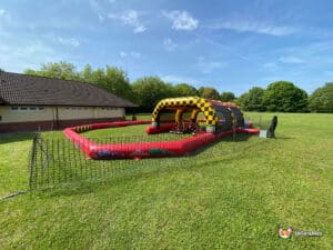 A large inflatable obstacle course in a field, styled as a race track, inviting participants for a fun-filled competition.