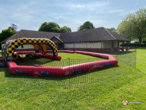 An expansive inflatable obstacle course resembling a race track, situated in a grassy field for outdoor entertainment.